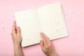 Female hands notebook and hydrangea flower petals on pink background