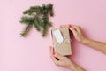Female hands, placing gift box next to fir branch over pink background