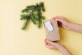 Female hands, placing gift box next to fir branch over yellow background