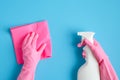 Female hands in pink gloves holding cleaning spray bottle and sanitary napkin on blue background. House cleaning or housekeeping Royalty Free Stock Photo