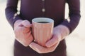 Female hands in pink mittens holding cup with hot tea or coffee. Close up