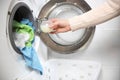 Female hands pouring liquid laundry detergent into measure cup. Washing machine and clothes in white modern room Royalty Free Stock Photo