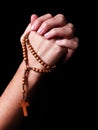 Female hands praying holding a beads rosary with a cross or Crucifix on black background Royalty Free Stock Photo