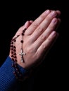 Female hands praying holding a rosary with Jesus Christ in the cross or Crucifix on black background. Royalty Free Stock Photo