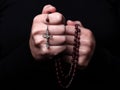 Female hands praying holding a rosary with Jesus Christ in the cross or Crucifix on black background.