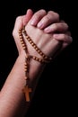 Female hands praying holding a rosary with Jesus Christ in the cross or Crucifix on black background. Royalty Free Stock Photo