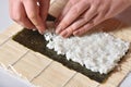 Female hands prepare homemade sushi roll and lay rice on nori leaf