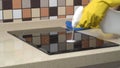 Female hands in protective gloves cleaning the surface of an induction cooker.