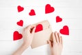 Female hands put red hearts in a congratulatory envelope on a white wooden background, happy valentine s day background Royalty Free Stock Photo