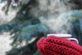 Female hands in red knitted mittens holding steaming cup of hot coffee or tea near fir christmas tree. Winter time concept. Royalty Free Stock Photo