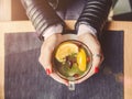 Female hands with red manicure holding cup of tea with herbs and lemon on table in cafe. Royalty Free Stock Photo