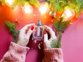 Female hands with red nails hold bottle of perfume. Branches of christmas fir tree, magic lights and pieces of golden paper on red Royalty Free Stock Photo