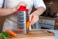 Female hands are rubbing fresh orange carrots on a steel silver grater. Grated carrots. Woman Chef prepares ingredients for