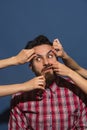 Female hands rumple young bearded handsome man on blue background