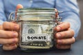 Female hands Saving Money In Glass Jar filled with Dollars banknotes. DONATE transcription in front of jar. Managing Royalty Free Stock Photo