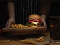 Female hands serving fresh tasty homemade burger with French fries and beverage Royalty Free Stock Photo