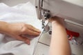 Female hands at sewing process and repairing white fabric on professional manufacturing machine. Close up macro view.