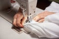 Female hands at sewing process and repairing white fabric on professional manufacturing machine. Close up top view.