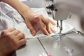 Female hands at sewing process and repairing white fabric on professional manufacturing machine. Close up view. Royalty Free Stock Photo