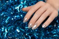 Female hands with silver Christmas nail design. Silver nail polish manicured hands. Female holding blue New Year tinsel