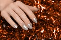 Female hands with silver Christmas nail design. Silver nail polish manicured hands. Female holding red New Year tinsel