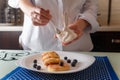 Female hands spkinkling honey on traditional syrniki or cottage cheese pankaces with blueberries and honey on white plate