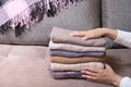 Female hands stack cozy knitted sweaters on the sofa with blanket. Warm concept