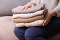 Female hands stack cozy knitted sweaters on the sofa. Warm concept