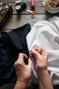 Female hands stitches black and white fabric on wooden table, scissors, casket, thread, glasses Royalty Free Stock Photo