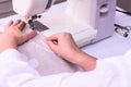 Female hands stitching white fabric on machine. Seamstress hands holding textile for linen.