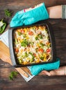 Female hands take baked pasta with broccoli and cheesy tomato sauce on wood background Royalty Free Stock Photo