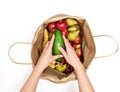 Female hands take out an avocado from a paper bag full of different fruits isolated on a white background. Delivery and purchase Royalty Free Stock Photo