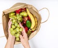 Female hands take out a bunch of grapes from a paper bag full of different fruits isolated on a white background. Delivery and Royalty Free Stock Photo