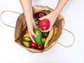 Female hands take out a red apple and avocado from a paper bag full of different fruits isolated on a white background. Delivery Royalty Free Stock Photo