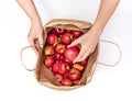 Female hands take out a red apple from a paper bag full of red ripe fragrant fresh apples, isolate on a white background. Royalty Free Stock Photo