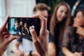 Female hands taking photo with smartphone of young cheerful friends, blurred background