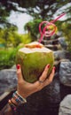 Female hands in tattoos hold a coconut with a tubule in Thailand`s tropical garden. modern style of rest