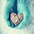 Female hands in teal knitted mittens with a entwined vintage romantic heart on a snow background. Love and St. Valentine concept Royalty Free Stock Photo