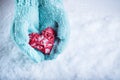 Female hands in teal knitted mittens with a entwined vintage romantic heart on a snow background. Love and St. Valentine concept