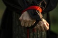 Female hands tied with a red rope. The victim is in the woods by the tree. Crime and aggression. Close-up. Low key