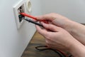 female hands use the probes of a digital multimeter to check the current voltage in an electrical outlet