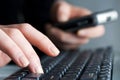 Woman using computer keyboard and calling on cell phone Royalty Free Stock Photo