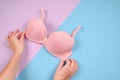 Female hands on a violetand blue background holding a beautiful pink bra. Daily underwear concept. Sales concept