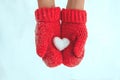 Female hands in warm red crocheted mittens with snowy heart. Whi Royalty Free Stock Photo