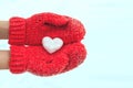 Female hands in warm red crocheted mittens with snowy heart. Whi