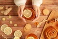 Female hands in warm sweater holding cup of tea with lemon, honey, ginger root ingredients and sweet cinnamon bun on Royalty Free Stock Photo