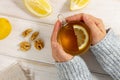 Female hands in warm sweater holding cup of tea with lemon on white wooden table