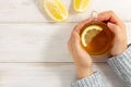 Female hands in warm sweater holding cup of tea with lemon on white wooden table