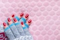 Female hands in warm winter knitted gloves with patterns with beautiful manicure - red glittered nails on pink fluffy