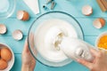 Female hands whipping egg whites cream in glass bowl with mixer on blue wooden table. Royalty Free Stock Photo